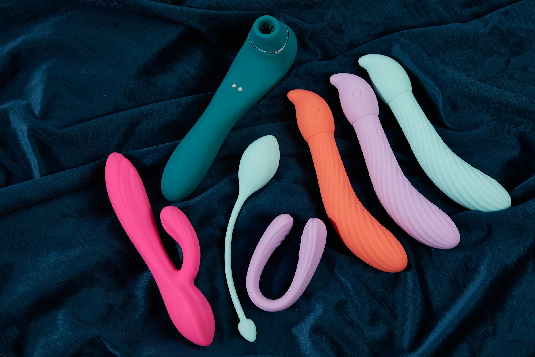 Colorful silicone clitoral vibrators arranged on dark blue fabric, representing diverse pleasure tools
