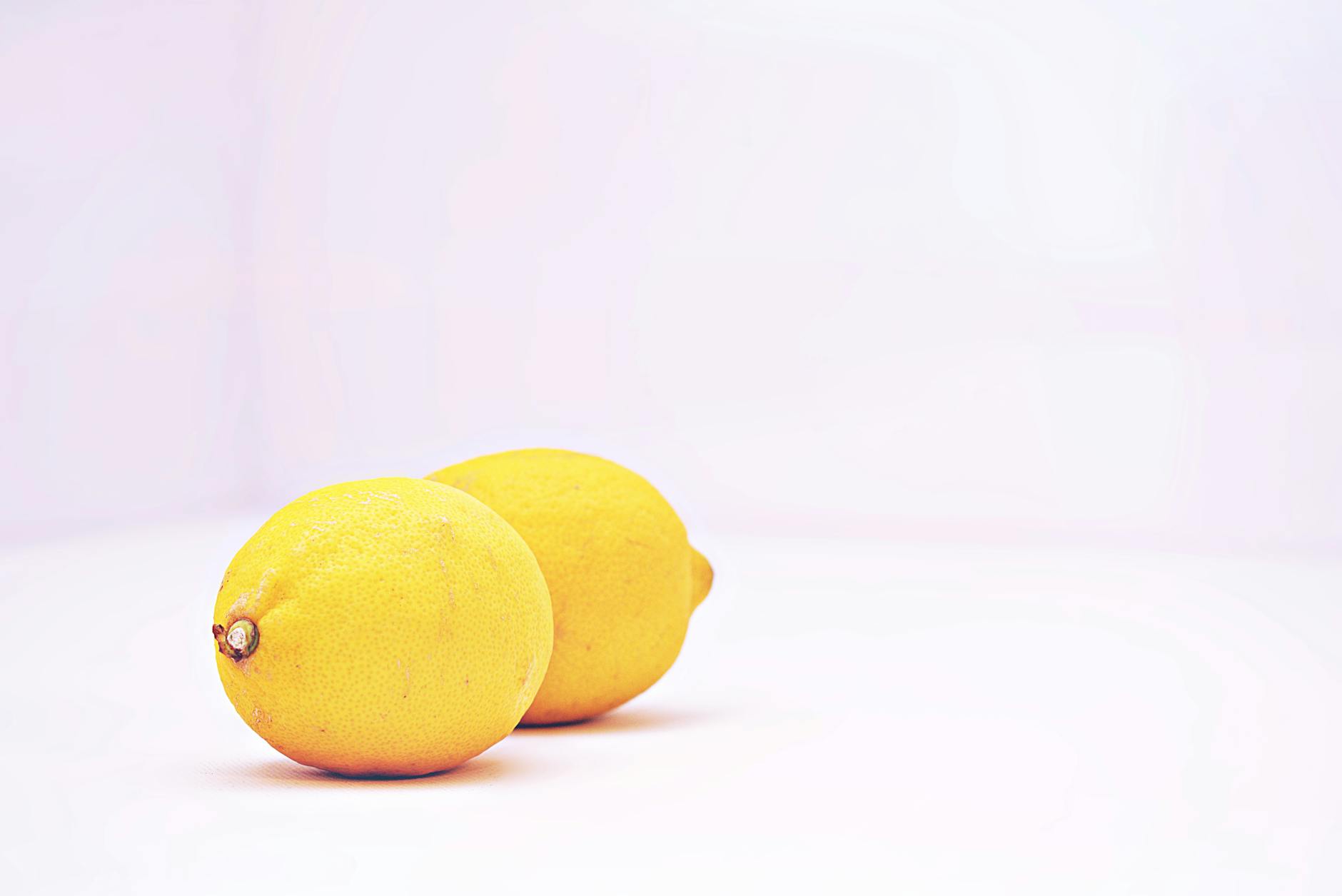 Hand holding a fresh lemon on soft pink background with additional lemons