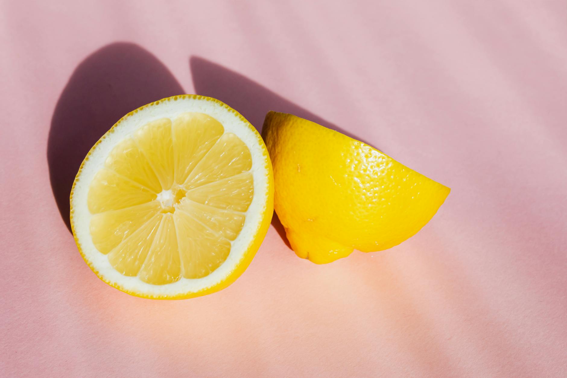 Close-up of fresh lemon halves on a pink background, symbolizing the bright sensation of clitoral stimulation