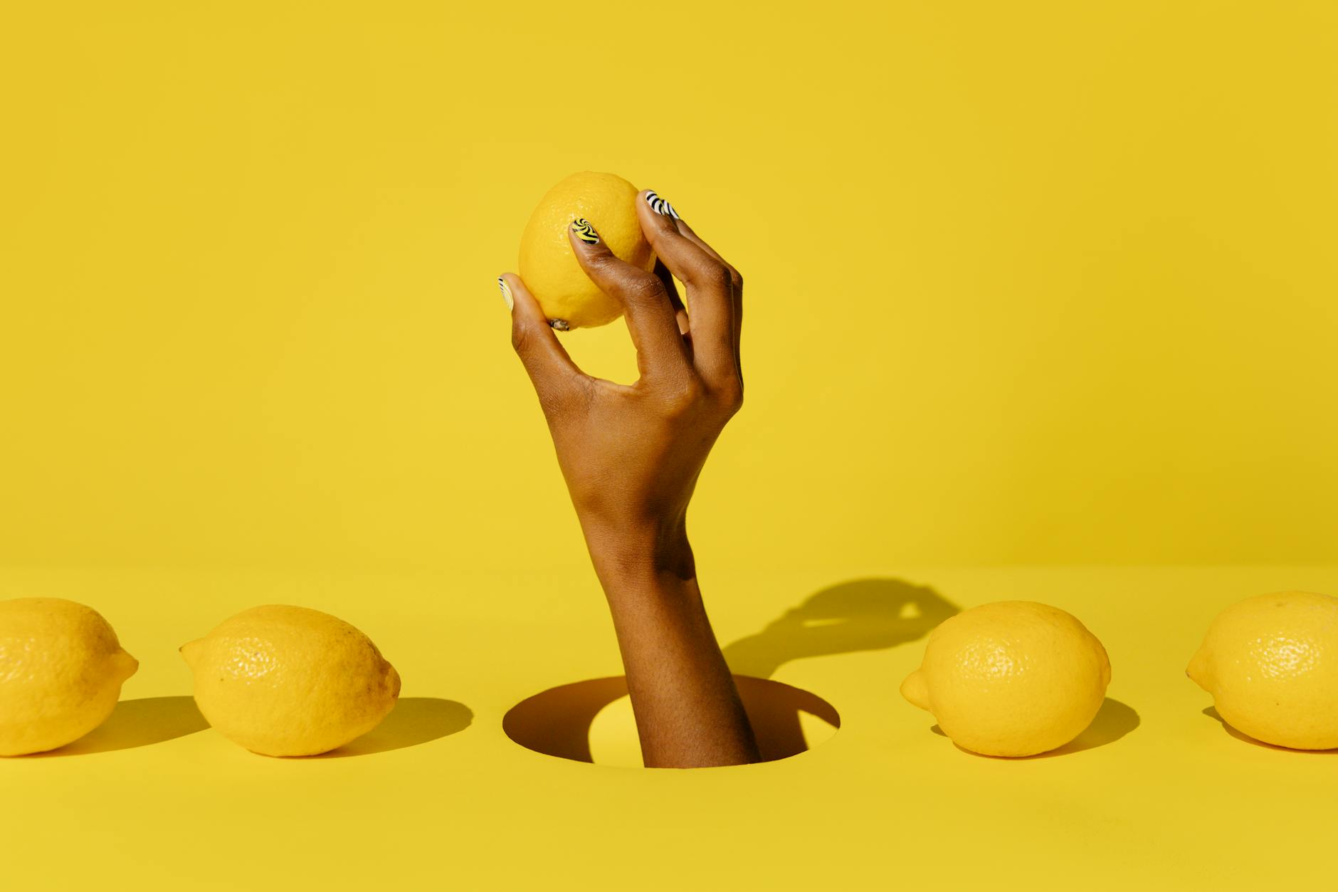 A hand holding a fresh lemon against a yellow background, symbolizing the vibrant sensation of the Lem lemon vibrator