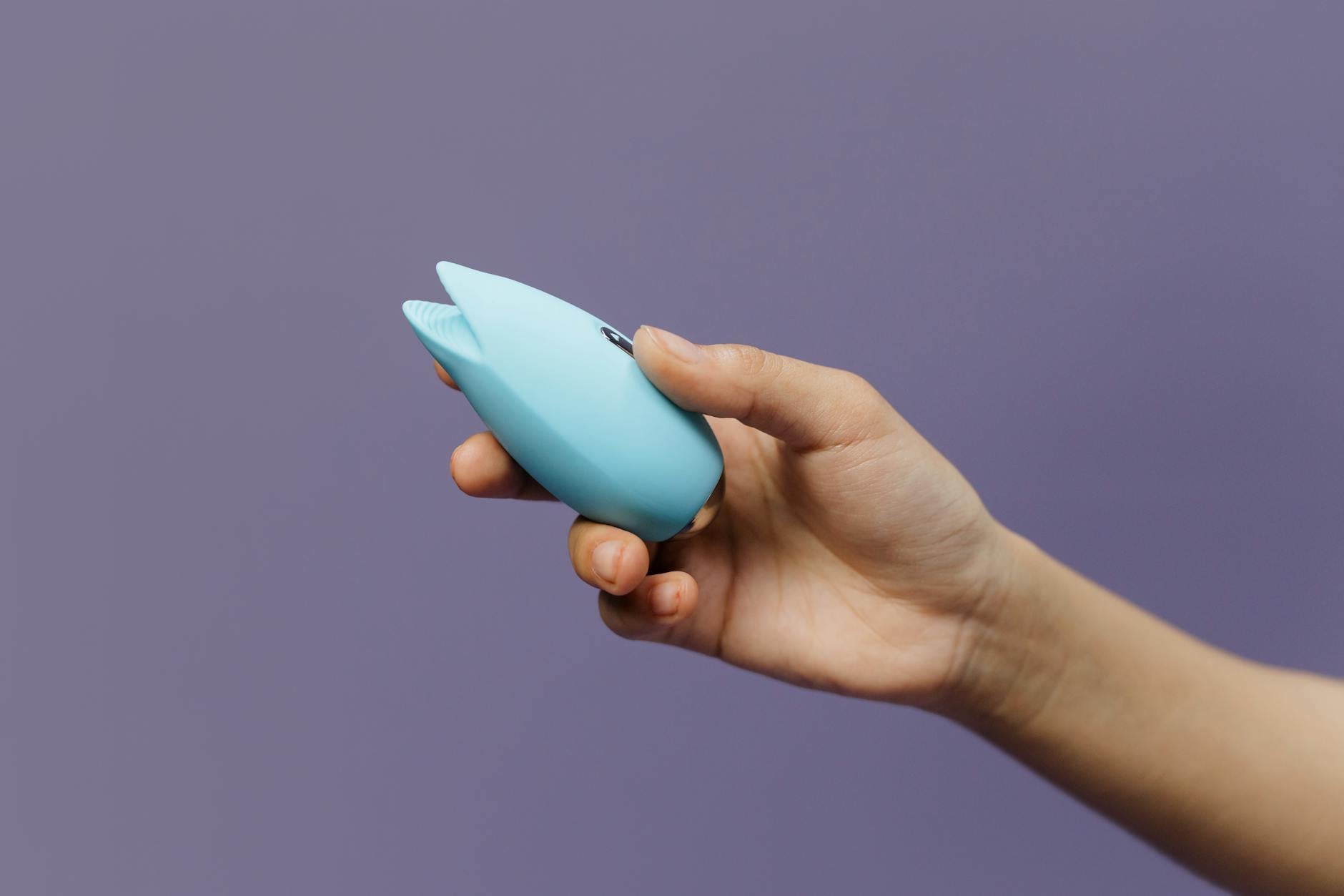 A hand holding a lemon-shaped vibrator against a purple background