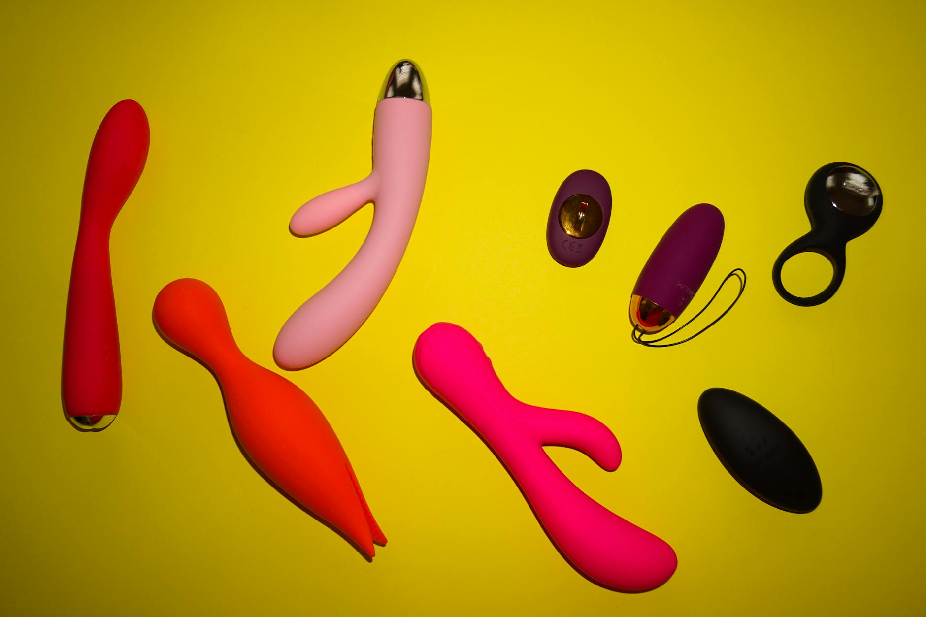 Collection of colorful clitoral vibrators and lemon toys arranged on a bright yellow surface